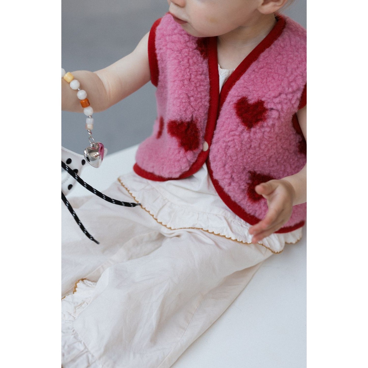 Alwero X Salty Lulu Baby bodywarmer roze met hartjes, baby draagt vest terwijl speelgoed vasthoudt