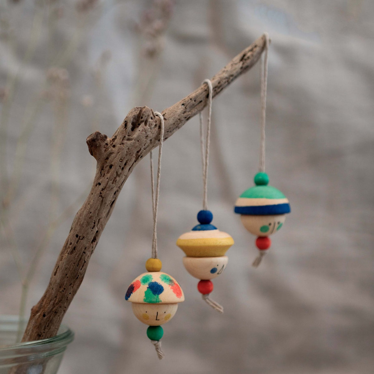 KIND FOLKS houten hangers aan drijfhout tak, drie gekleurde speelgoedfiguren hangend tegen neutrale achtergrond