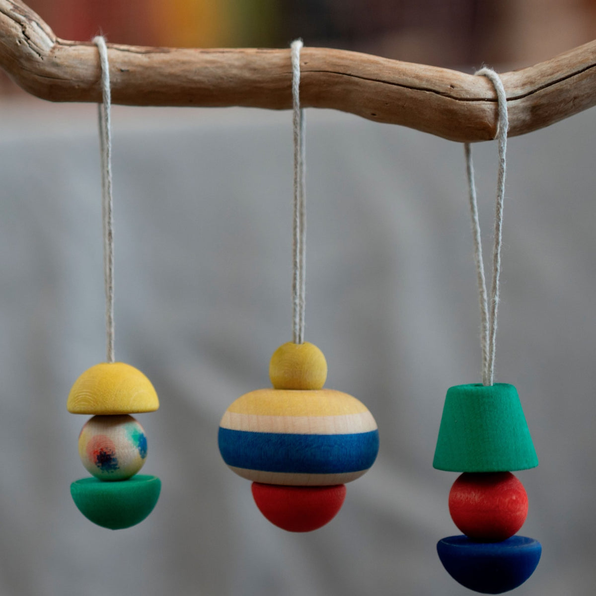 Drie houten hangers aan touw op een tak, elk samengesteld uit gekleurde houten blokken in verschillende vormen en stapeling