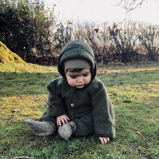 baby in het gras met wollen jas en sloffen