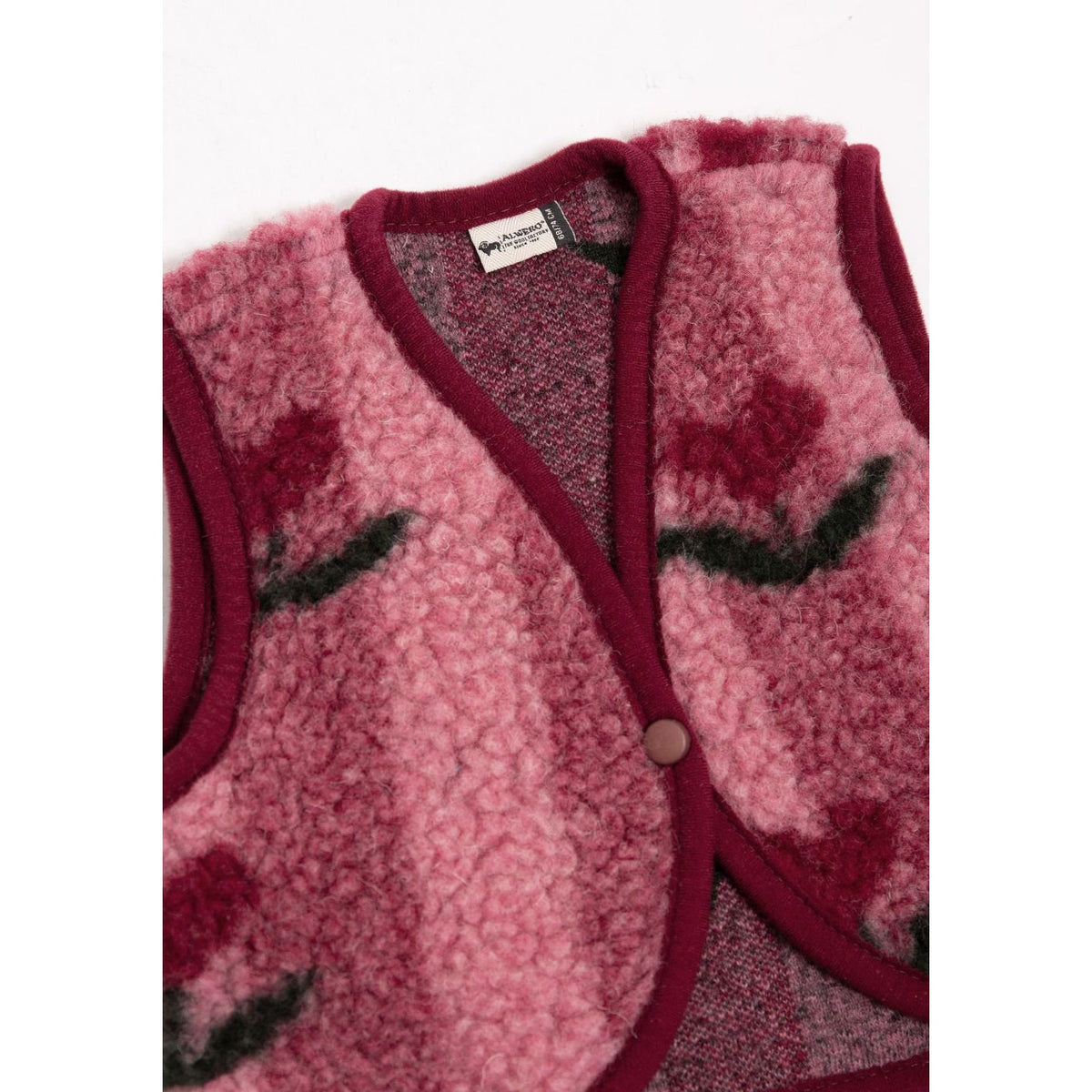 Lulu Baby bodywarmer in cherry roze met donkerrode ribkant, detail van gesloten voorkant met knoop en geborduurd gezichtsmotief