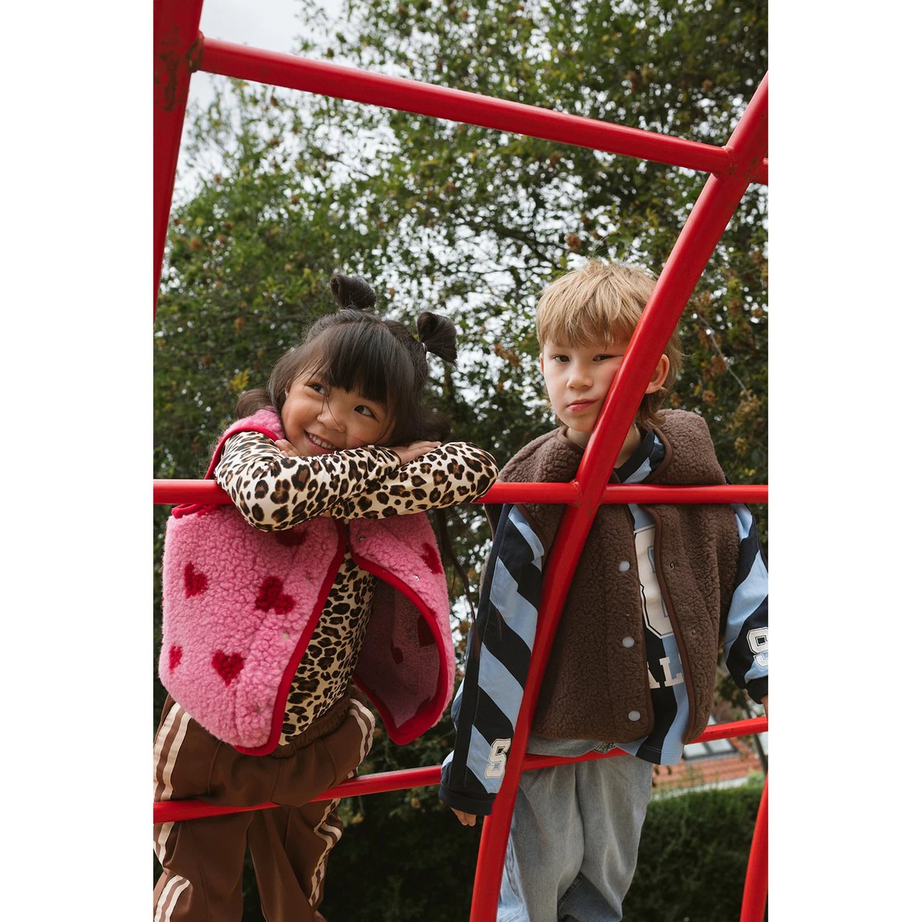 Alwero X Salty Tyb Junior Bodywarmer Bubble: twee kinderen op rode klimrek dragen wollen bodywarmers in bruintinten met patronen.