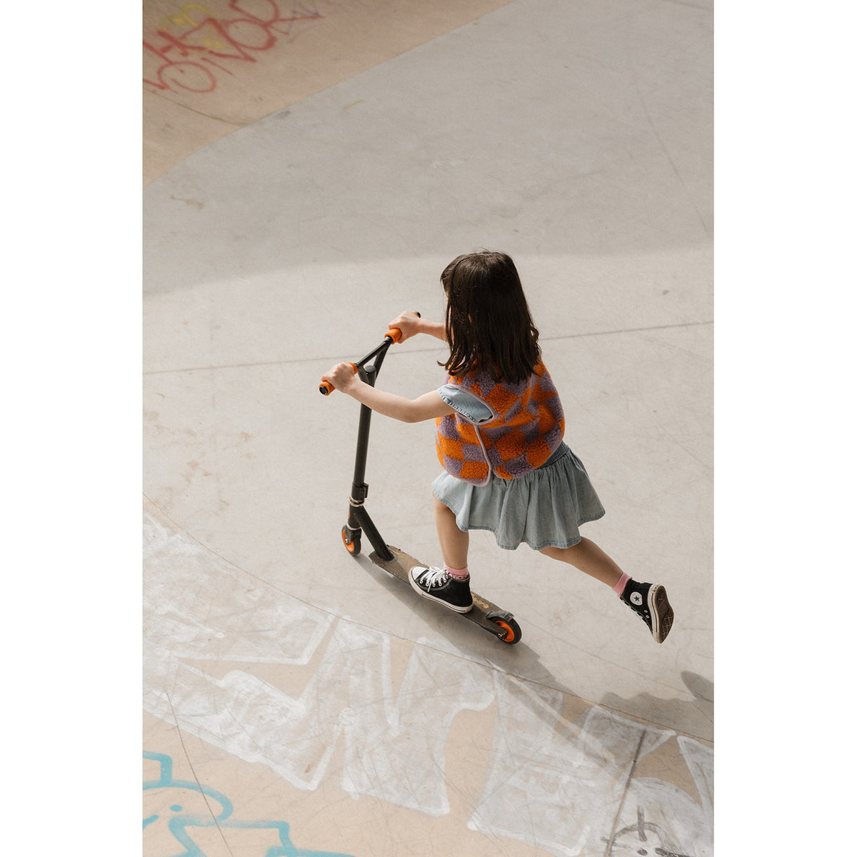 Alwero bodywarmer geblokt oranje: meisje rijdt op step in skatepark, bovenaanzicht