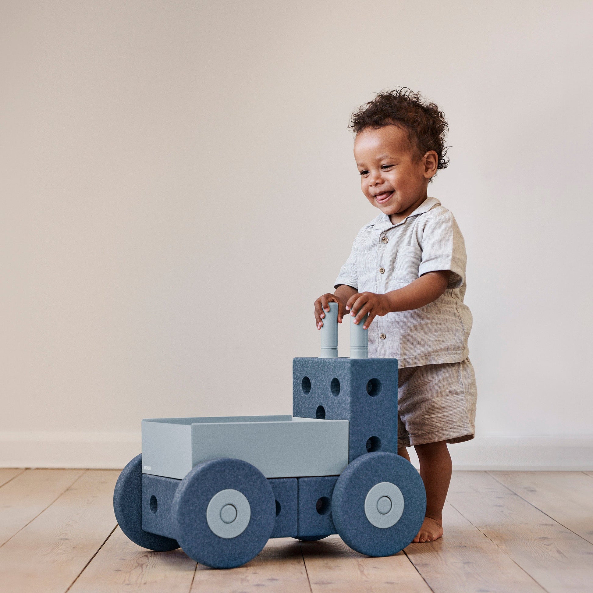 MODU 3-in-1 Baby Walker Deep Blue Sky Blue met peuter die tegen loopwagen leunt, frontaal zicht op wielen en blokkenstructuur