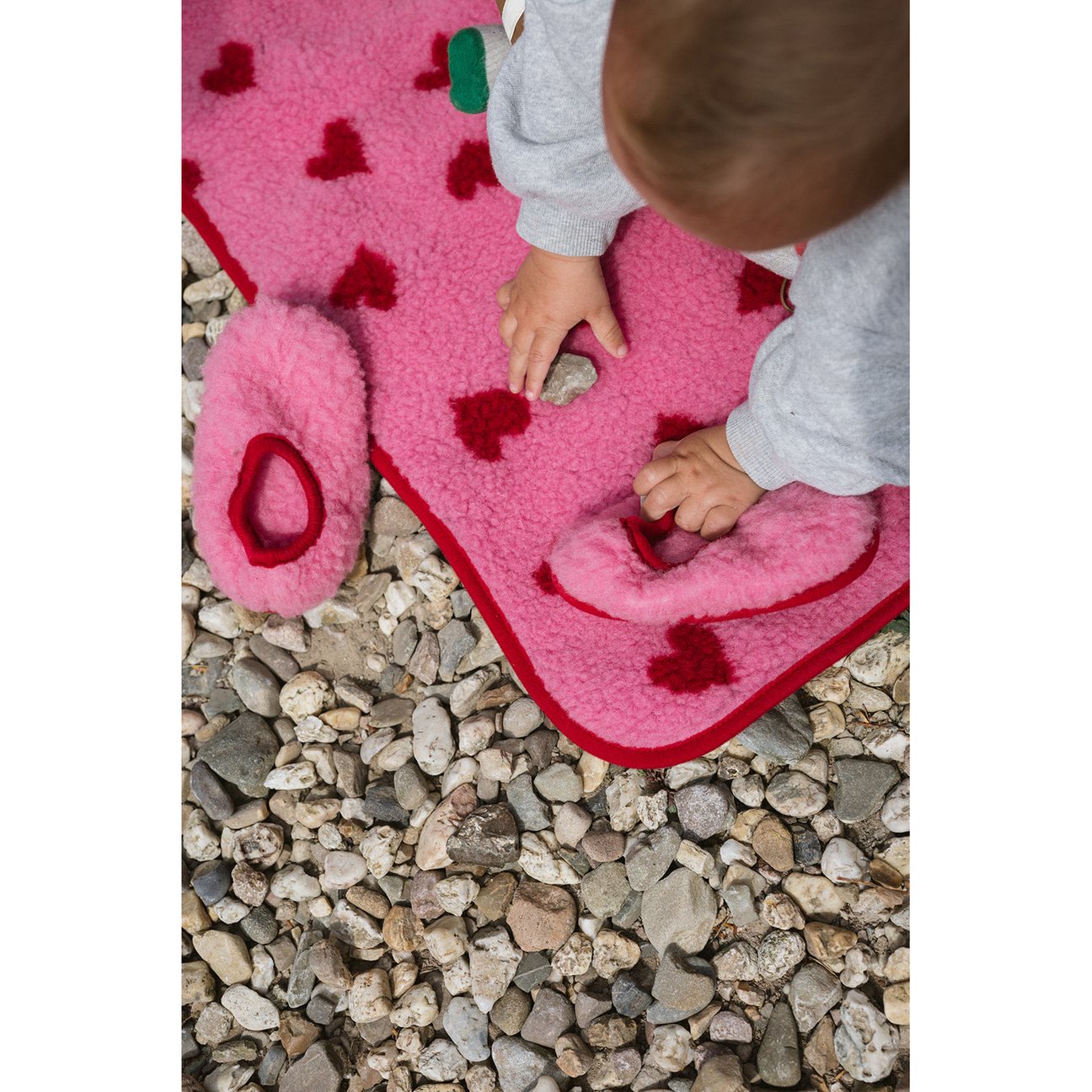 Alwero Thumbled wollen deken in roze met rode hartjes, gebruikt door baby op kiezelstenen ondergrond