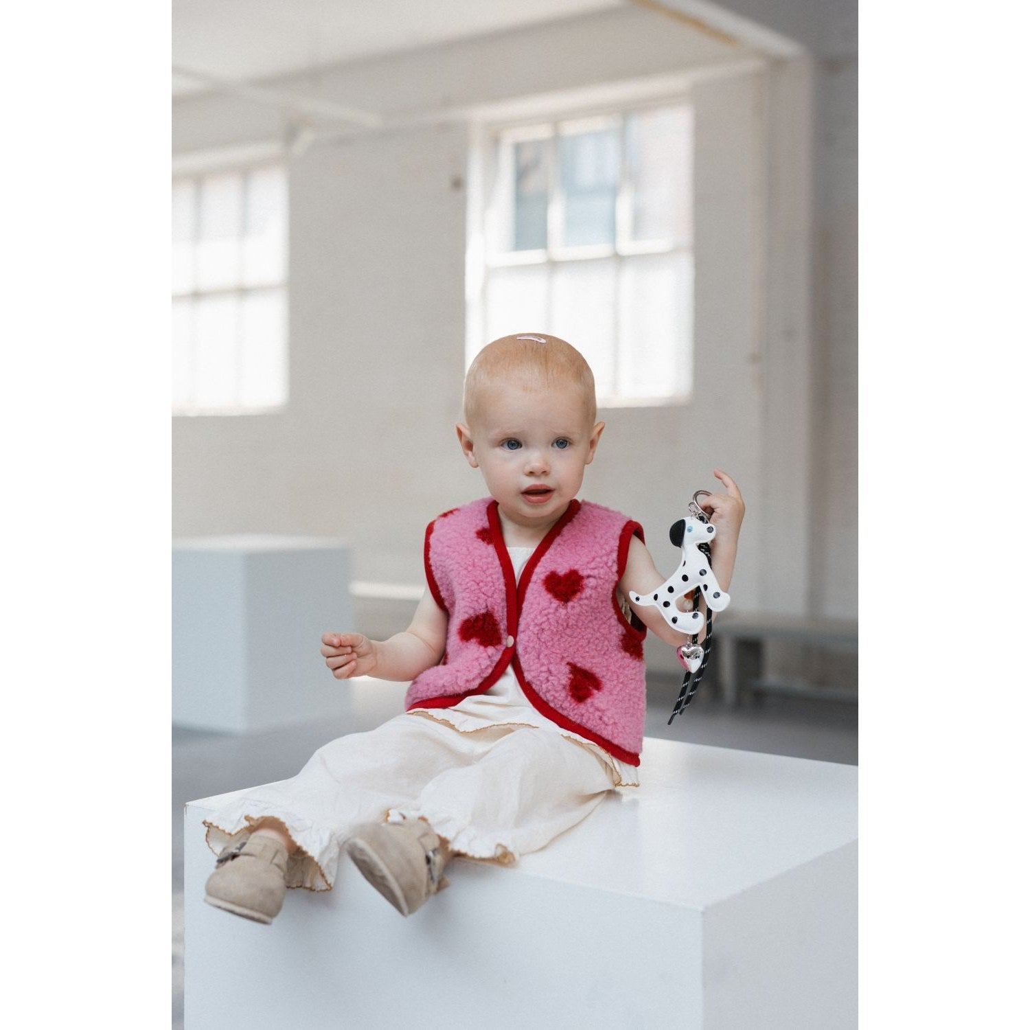 Alwero X Salty Lulu Baby bodywarmer roze met hartjes, gedragen door peuter op wit podium met speelgoed