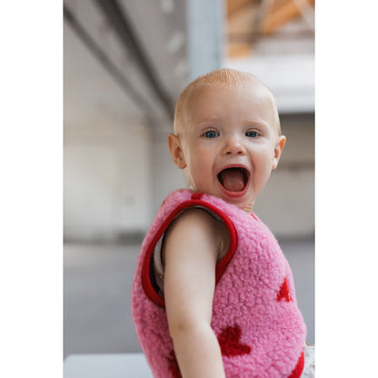 Alwero X Salty Lulu Baby bodywarmer: lachend peuter van achteren in roze wollen vest