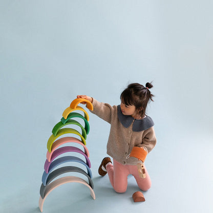 Avdar houten regenboog stacker: klein meisje stapelt 12 gekleurde bogen op hellend vlak tegen lichtblauwe achtergrond
