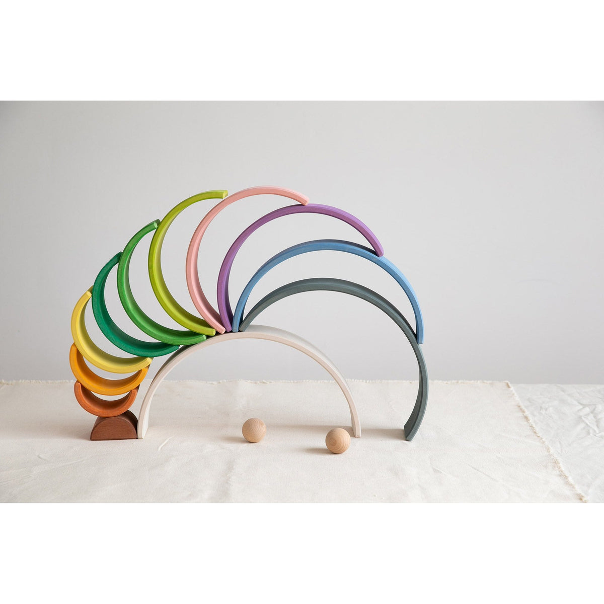 Avdar houten regenboog stacker met 12 gekleurde bogen in opstelling, twee houten balletjes ernaast