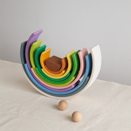 Avdar grote regenboog stacker opgesteld met geneste bogen, bruin bolletje centraal, twee losse houten balletjes ervoor op beige ondergrond