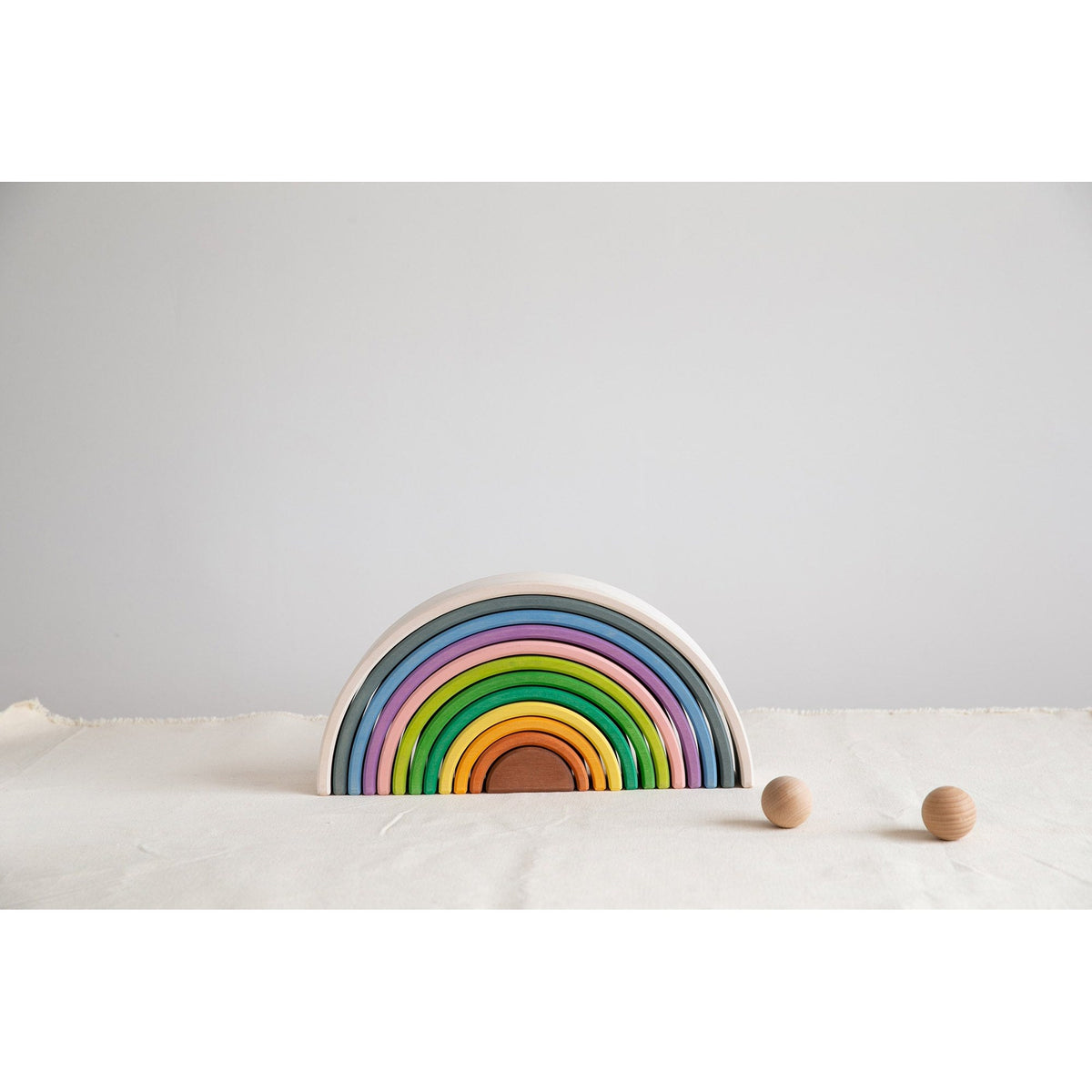 Avdar houten regenboog stacker in zand, half ingegraven met twee houten ballen ernaast