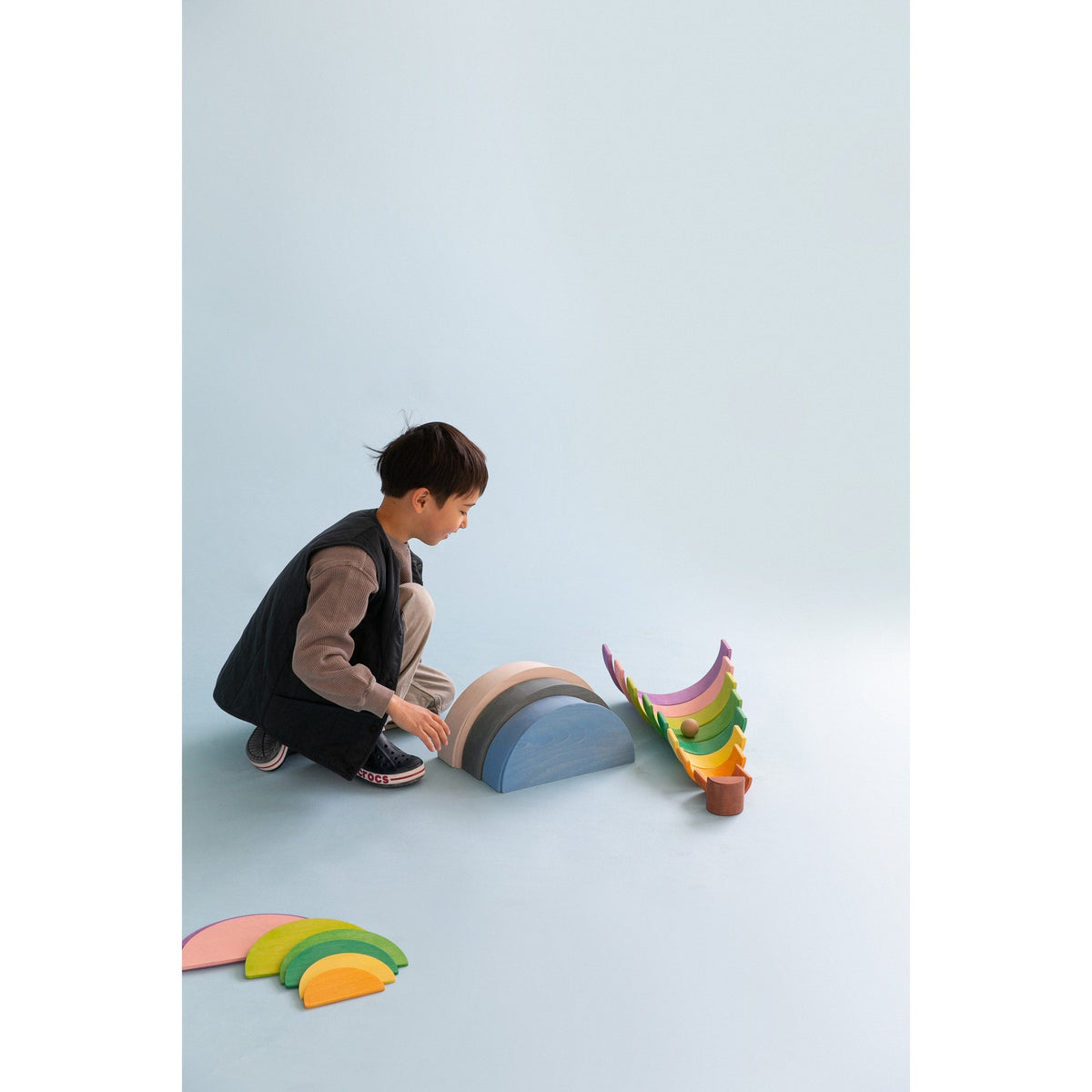 Kind speelt met Avdar houten halve cirkels in regenboogkleuren, zijaanzicht van bouwactiviteit