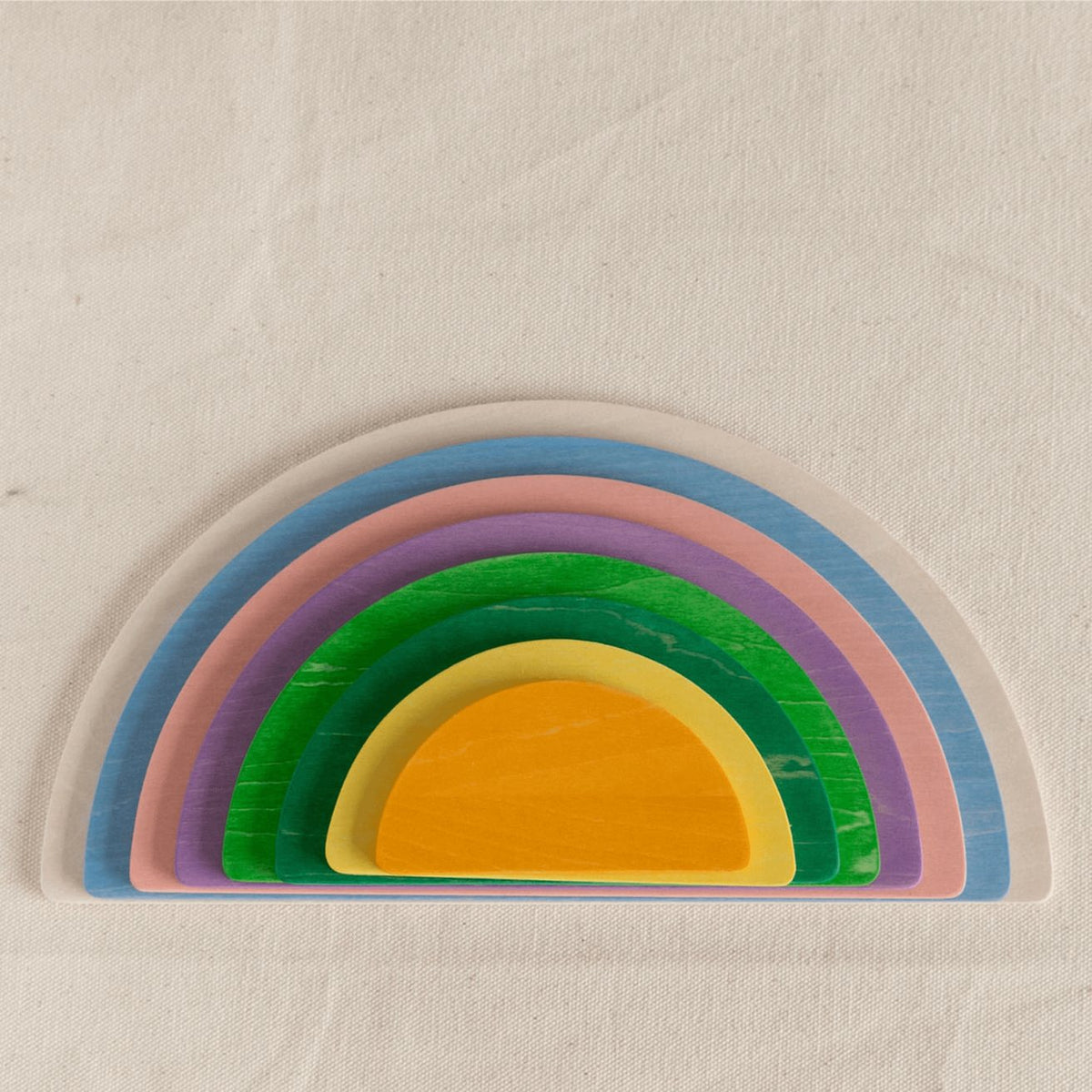 Avdar houten halve cirkels in regenboogkleuren gestapeld van groot naar klein, bovenaanzicht op naturel achtergrond