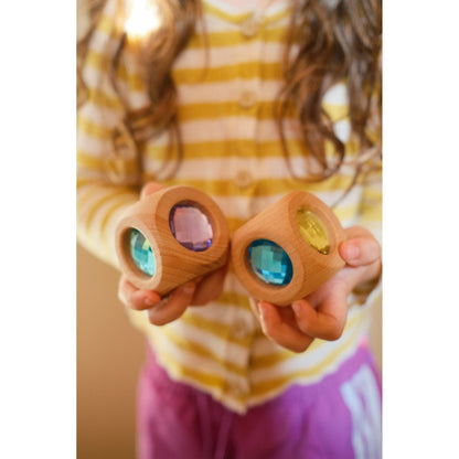 Kind houdt twee houten Bauspiel Magic Cube sensorische speelkubussen omhoog met gekleurde kristallen vensters