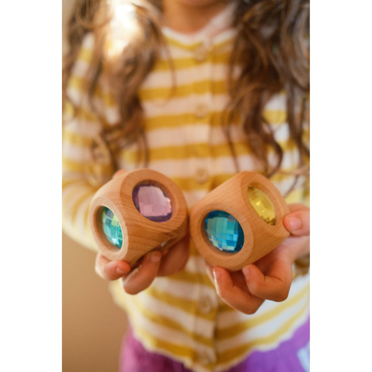 Bauspiel Magic Cube sensorische speelkubus in pastelkleuren, van dichtbij vastgehouden door kind met gestreepte gele shirt