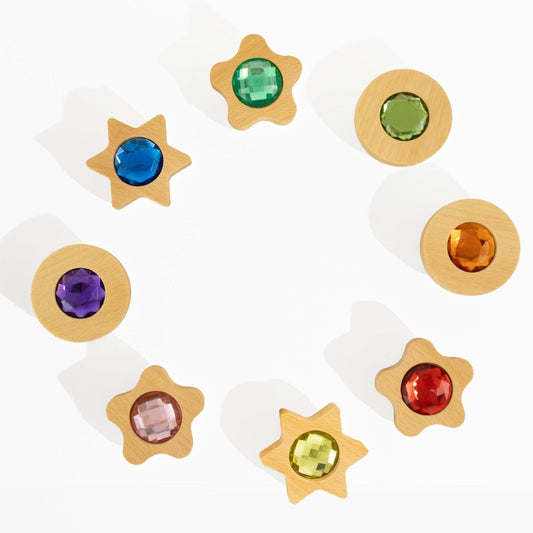 Bauspiel sensorische speelmunten met fonkelstenen in 8 kleuren, cirkel- en stervormig houten design tegen witte achtergrond.