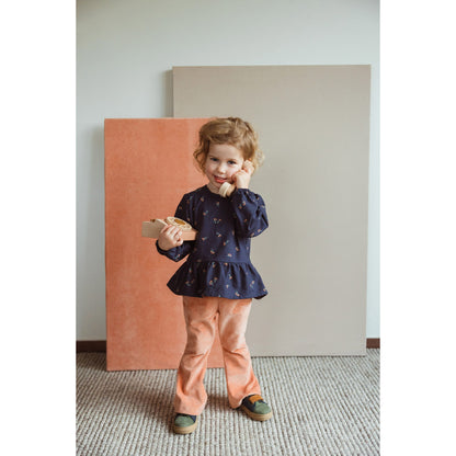 Wooly Organic blouse donkerblauw met bloemenprint, gedragen door klein kind in vol staand portret tegen gekleurde achtergrond