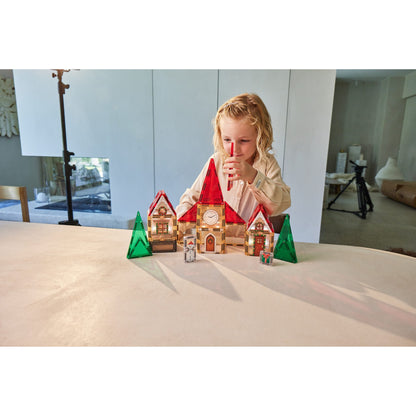 Cleverclixx Christmas Village adventskalender: kind speelt met verlicht magnetisch tegels-speelgoed kerkgebouw met rode daken en groene bomen op tafel