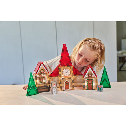 Cleverclixx Christmas Village adventskalender met 46 tegels: meisje bouwt verlicht kersthuis met rode torens en groene bomen.