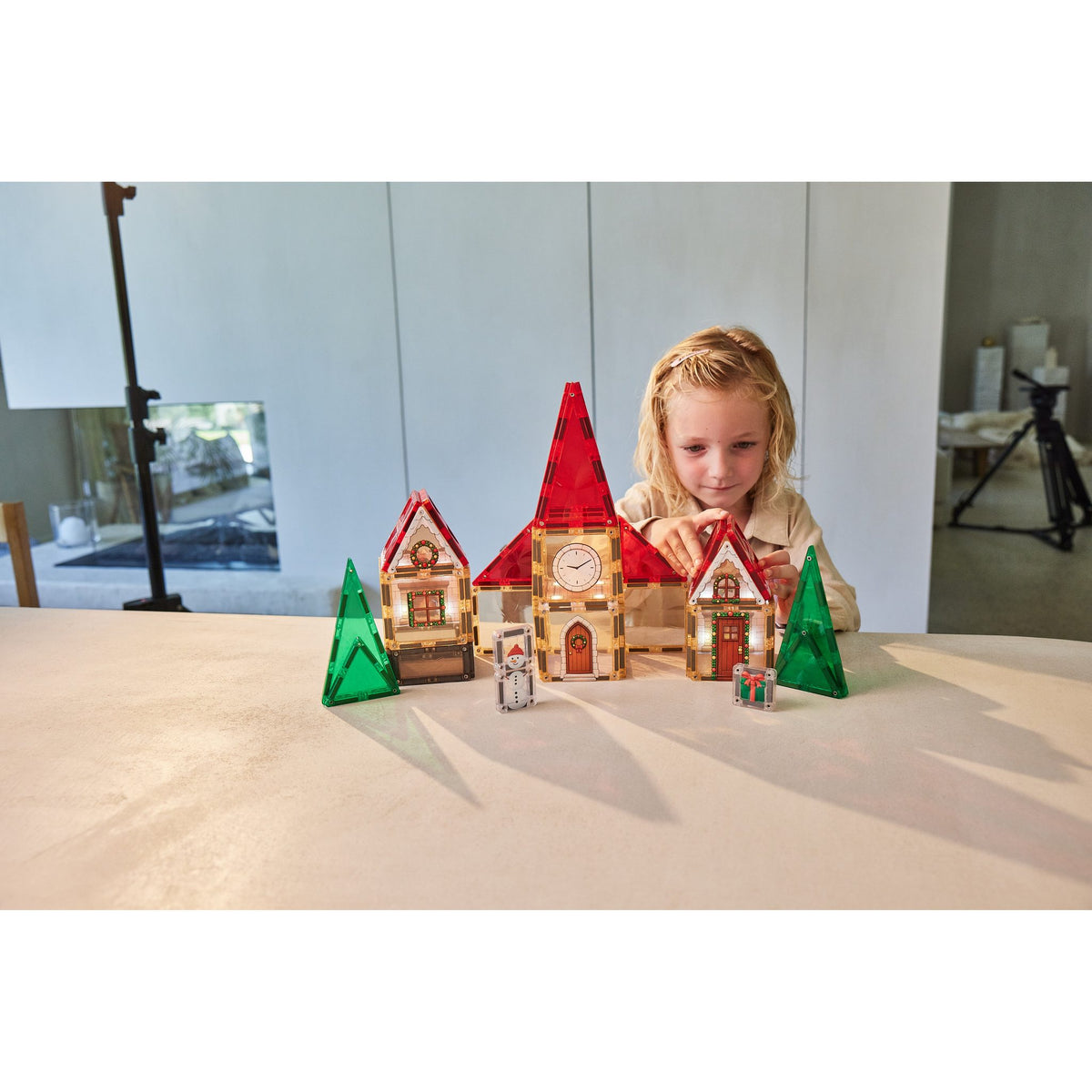 Cleverclixx Christmas Village adventskalender met magnetische tegels: meisje bouwt verlichte kerstdorp met rode daken en groene bomen op tafel