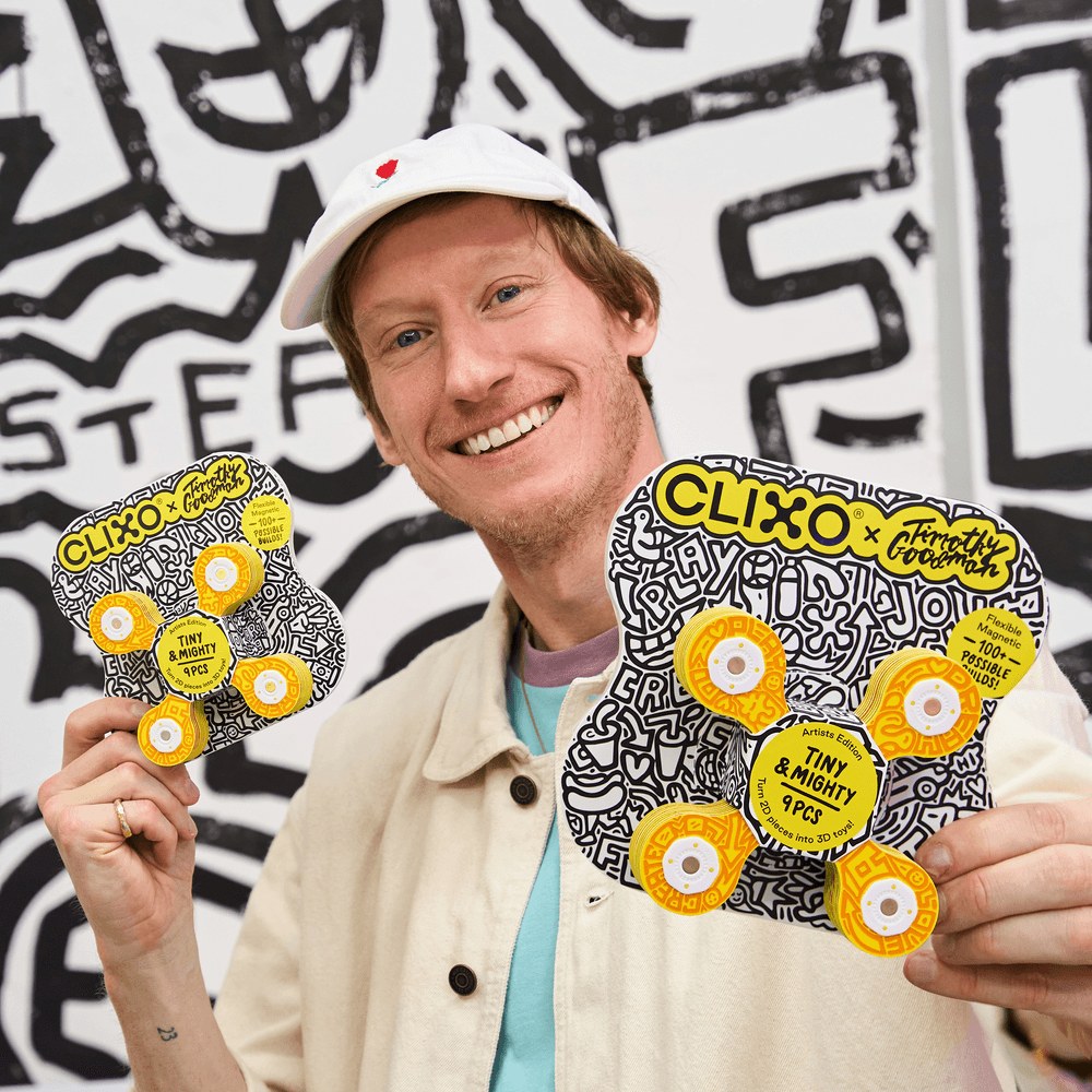 Clixo Tiny & Mighty Artist Edition: man met witte pet toont twee magnetische bouwsets met geel-zwart design van Timothy Goodman tegen graffiti achterg