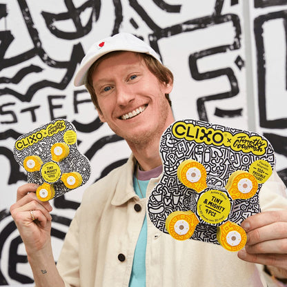 Clixo Tiny & Mighty Artist Edition: man met witte pet toont twee magnetische bouwsets met geel-zwart design van Timothy Goodman tegen graffiti achterg