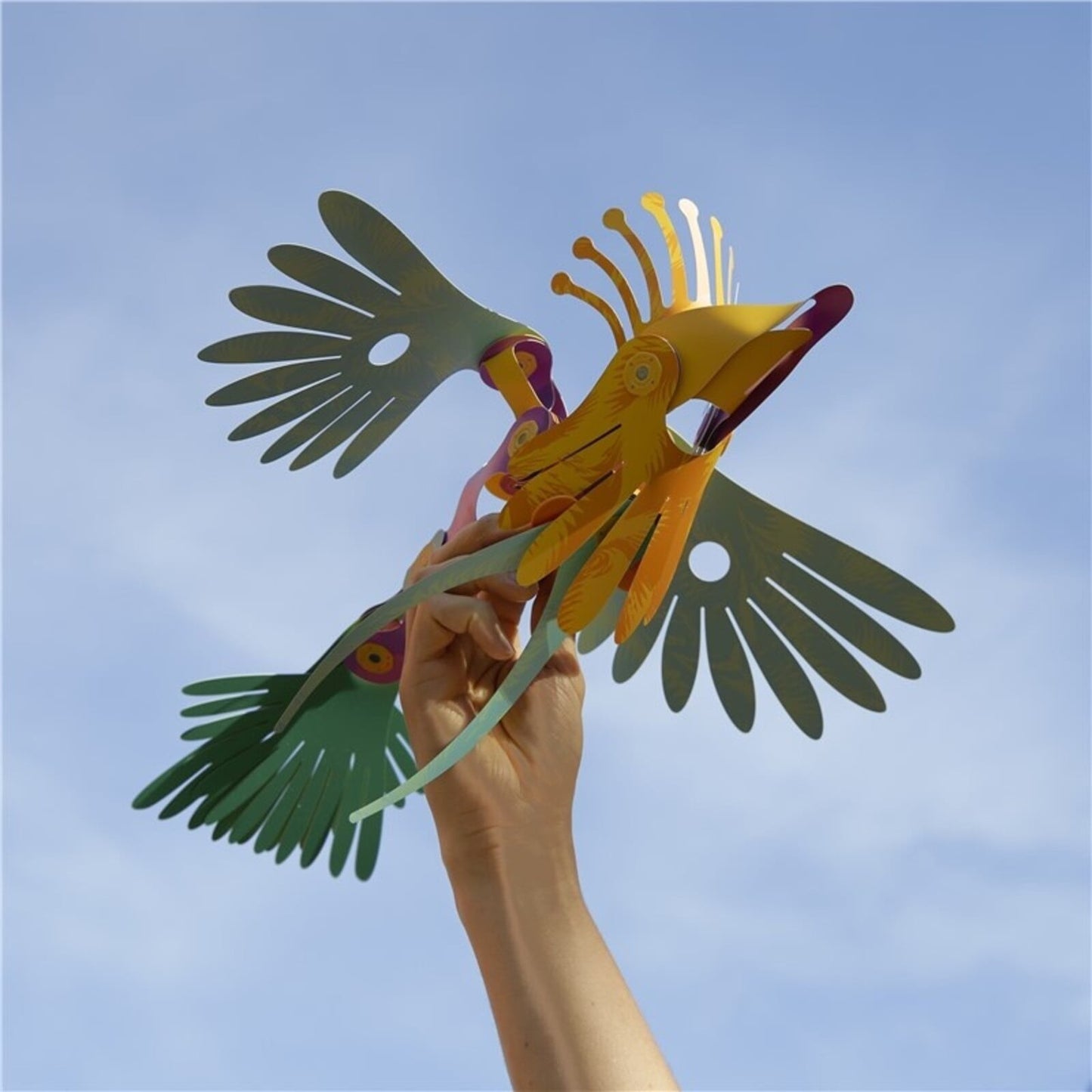 Clixo magnetische tropische vogel in geel en groen gehouden in hand tegen blauwe lucht, vleugels uitgespreid