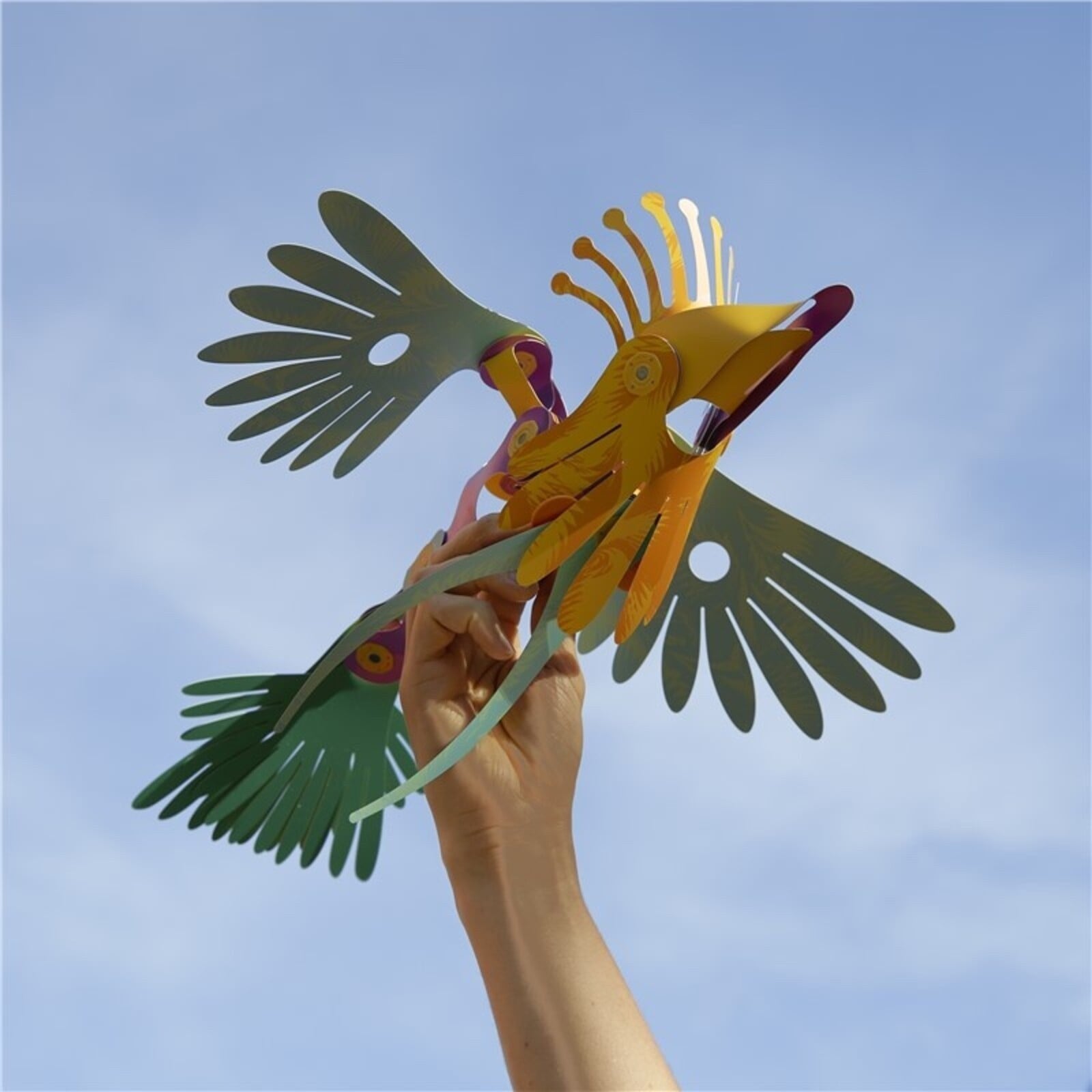 Clixo magnetische tropische vogel in geel en groen gehouden in hand tegen blauwe lucht, vleugels uitgespreid
