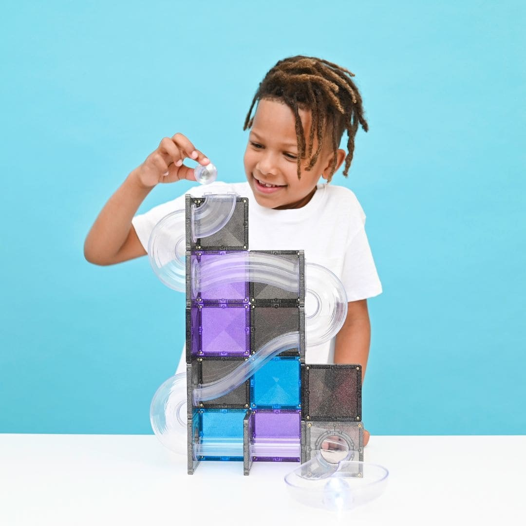 Kind bouwt Connetix Galaxy knikkerbaan met paarse en blauwe magnetische tegels, knikker bovenaan