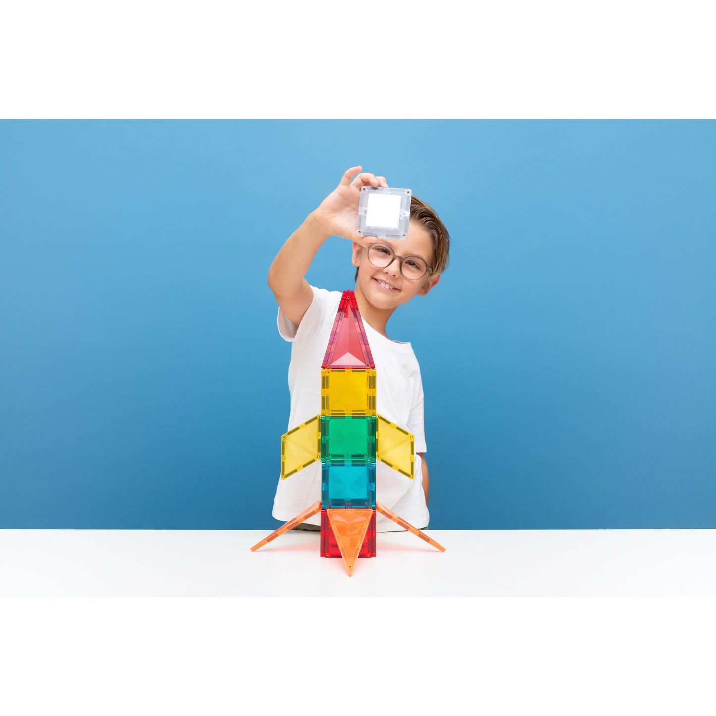 Jongen met bril houdt witte lichtegel omhoog boven Connetix Light Rocket magnetische tegels bouwset