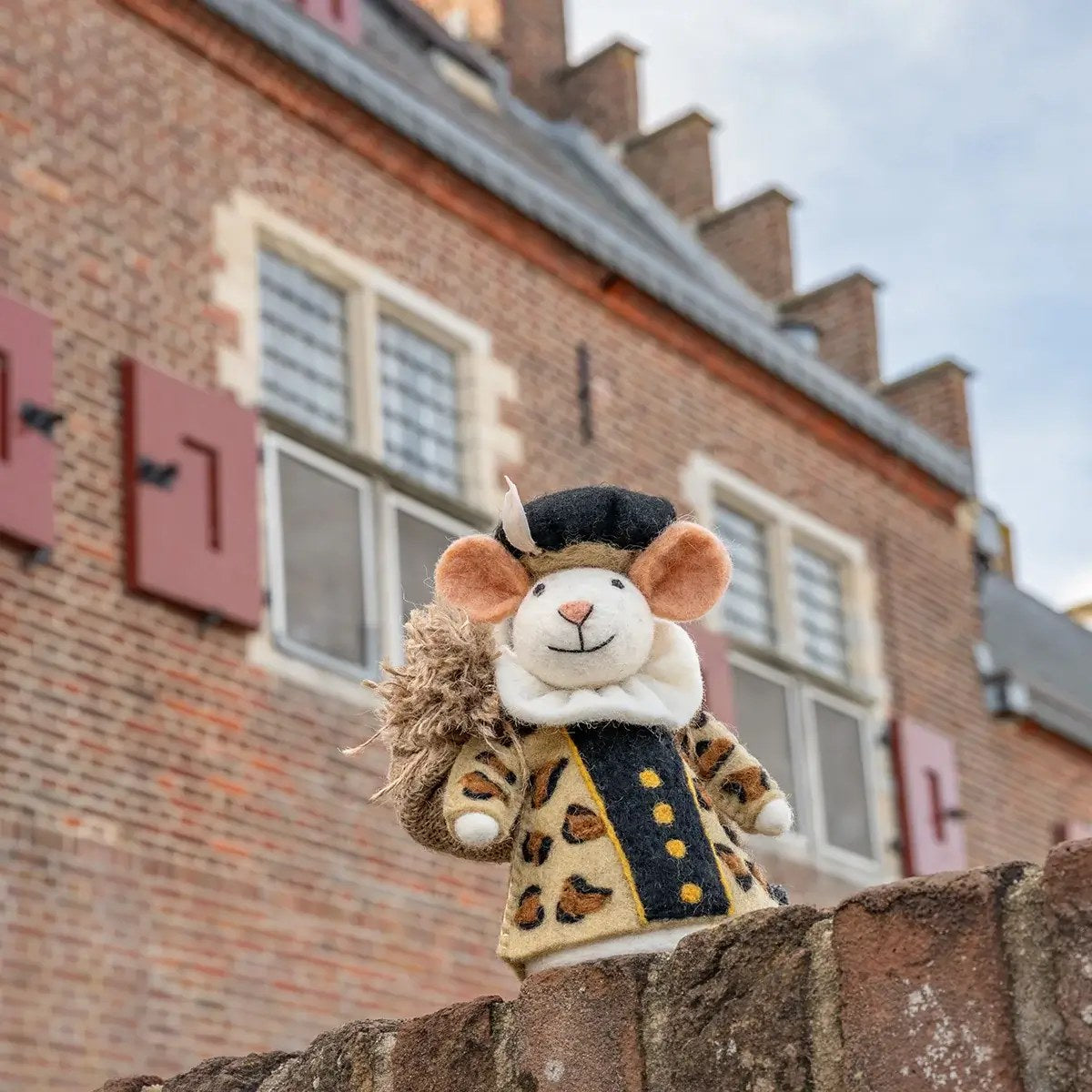 Sjaal met Verhaal decoratie muis Panterpiet van wolvilt, staand op stenen muur voor bakstenen huis