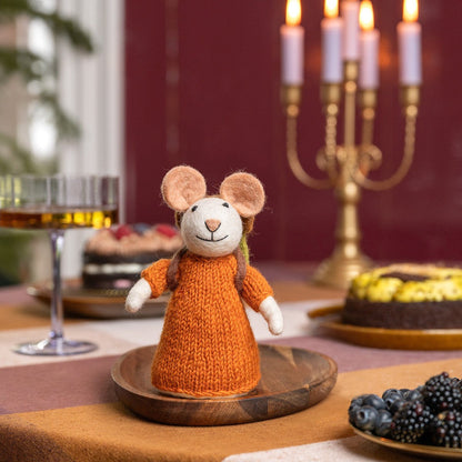 Sjaal met Verhaal decoratie muis in oranje gebreide trui op houten onderzettertje, staande op tafel met feestelijke achtergrond.