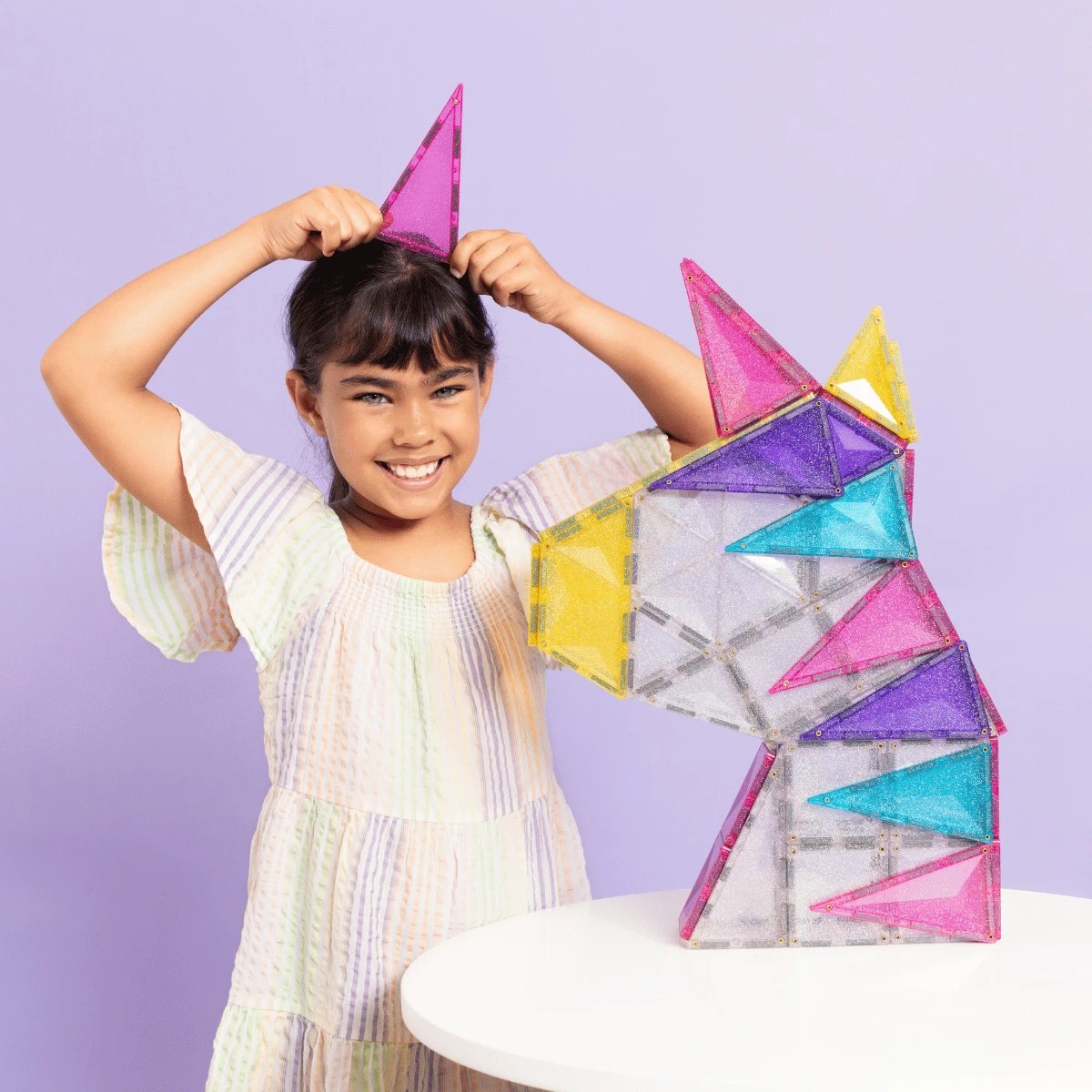 Connetix magnetische glitter tegels: meisje bouwt unicorn-kasteel met roze, gele, paarse en turquoise driehoeken.