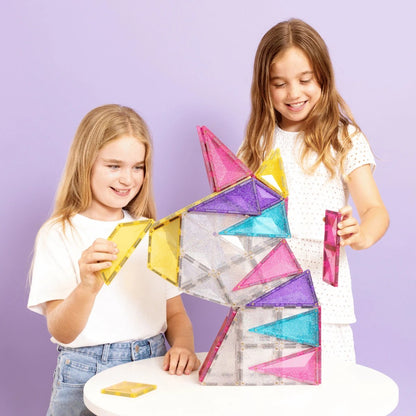 Connetix magnetische glitter tegels: twee meisjes bouwen een torenvormige structuur met gekleurde driehoekige stenen tegen paarse achtergrond.