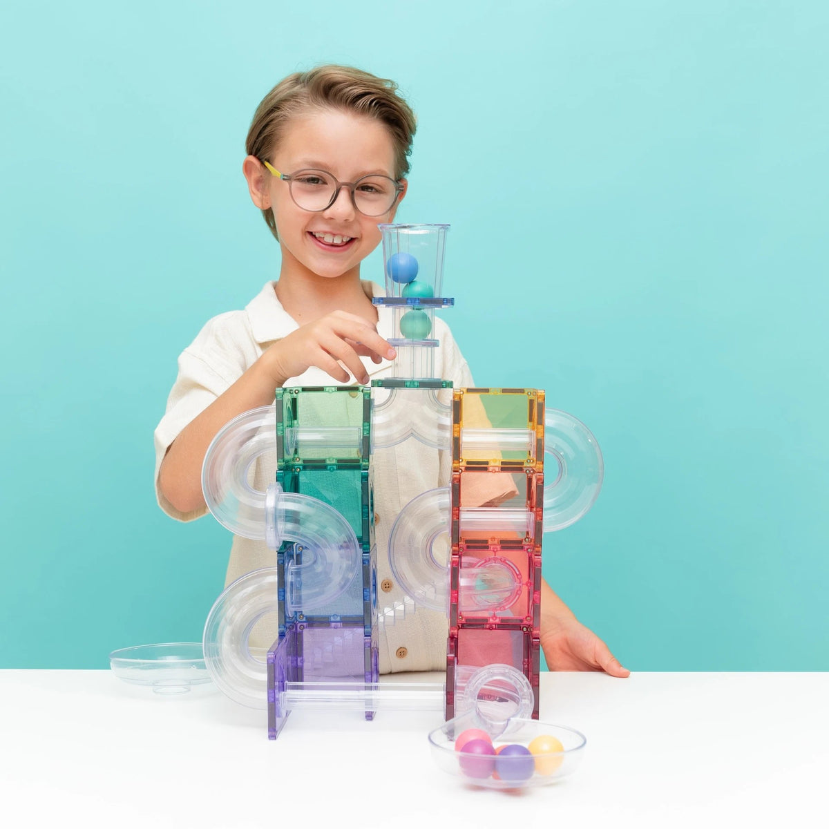 Kind speelt met Connetix magnetische balbaan in pastelkleuren, gebouw met gekleurde tegels en doorschijnende buizen