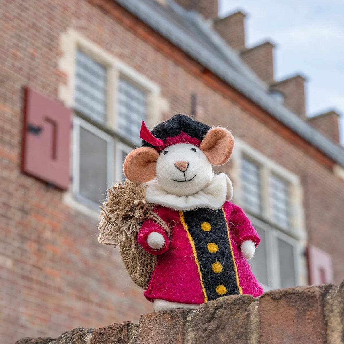 Sjaal met Verhaal Pietermuis in cyclaamrood piet kostuum met zwart jasje, frontaal gefotografeerd tegen bakstenen huisachtergrond