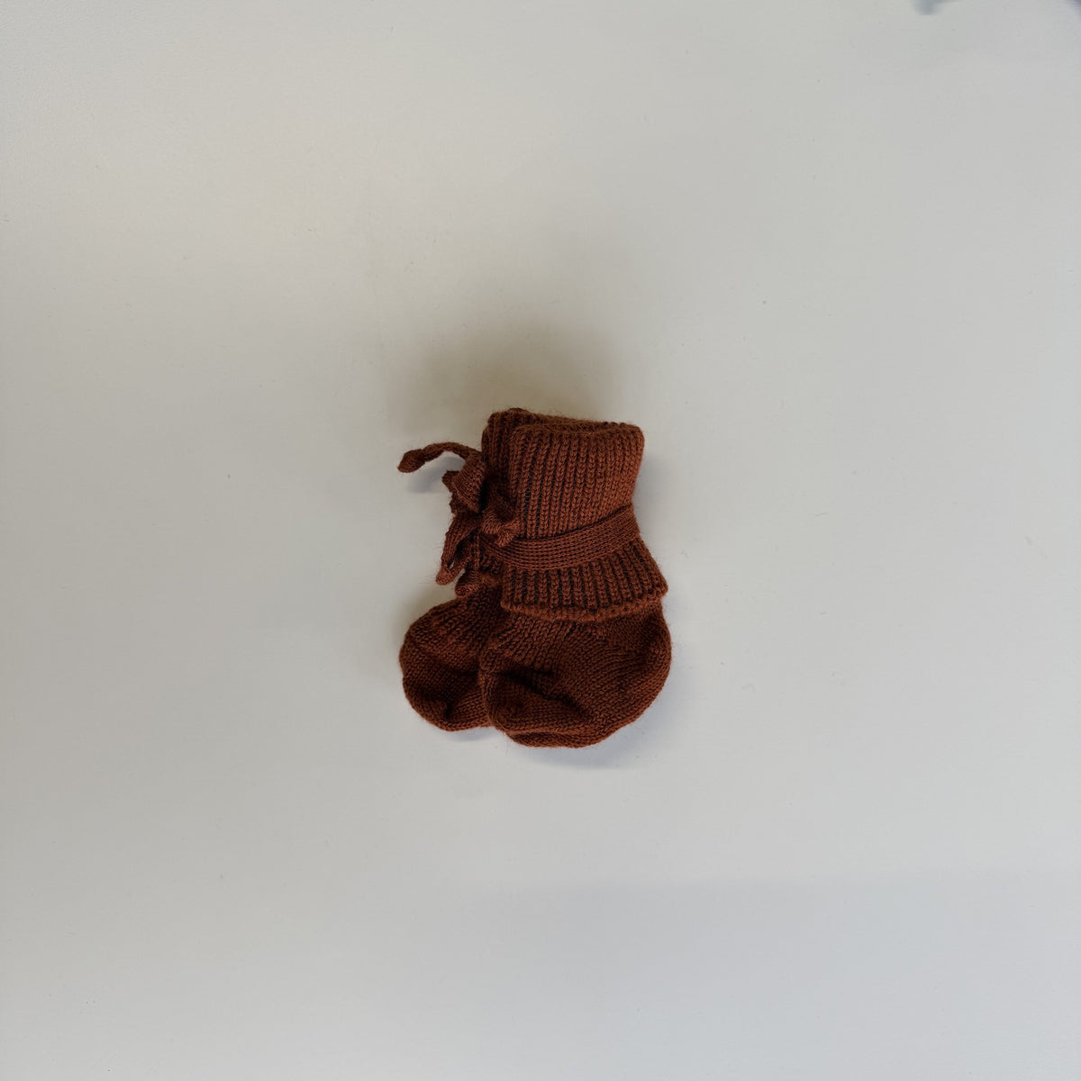 Hirsch Natur newborn sokjes in terracotta, gebreid, met strikje, bovenaanzicht op witte achtergrond