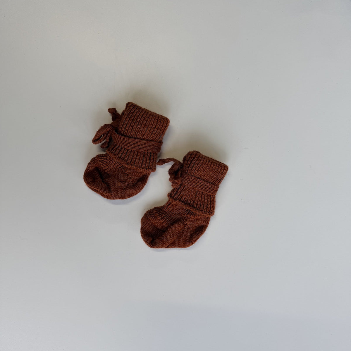 Hirsch Natur newborn sokjes in terracotta, twee paar getoond van bovenaf op witte achtergrond met duidelijke ribbelstructuur en strikjes