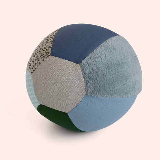 Little Botanic Label sensorische ballonbal met zeven verschillende stoftexturen in groen, blauw en beige tinten, weergegeven vanuit schuine hoek tegen