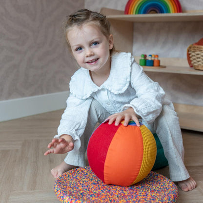 Little Botanic Label sensorische ballonbal in kleurrijke segmenten, vastgehouden door een peuter in speelkamer