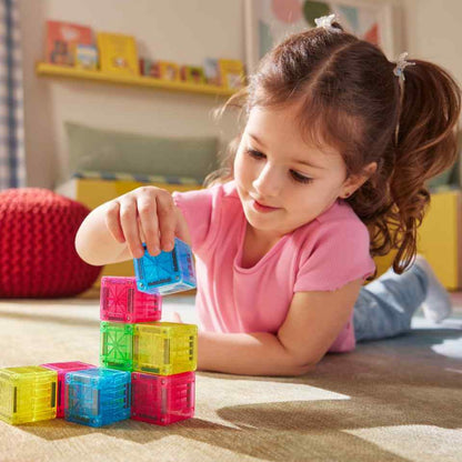 Meisje bouwt toren met Magna-Tiles MicroMAGS magnetische kubussen in roze, blauw en geel op speelmat.