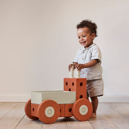 MODU 3-in-1 Baby Walker in Burnt Orange met klein kind staand achter loopwagen, frontaal zicht op modulair speelgoed met wielen