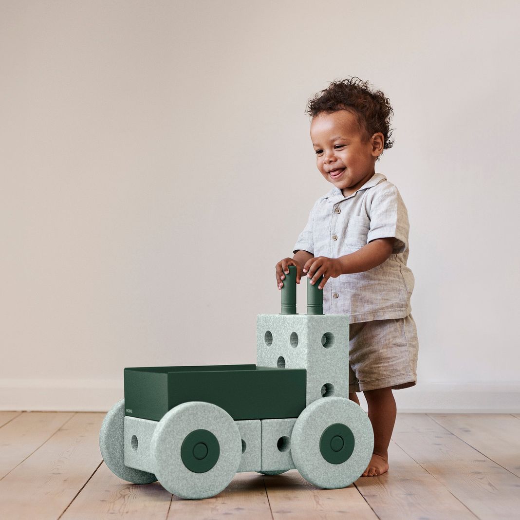 MODU 3-in-1 baby walker in ocean mint en forest green met peuter die erop speelt, frontaal zicht op het speelgoedvoertuig met wielen