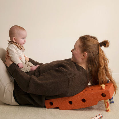 MODU Baby Activity Set in burnt orange gebruikt door moeder en baby op de grond - speelset met gaten en houten elementen zichtbaar