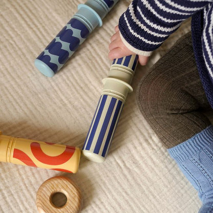 MODU Baby Activity Set Deep Blue onderdelen in gebruik: baby houdt blauwe gestreepte roller vast, met houten speeltjes en sensorische elementen op bei