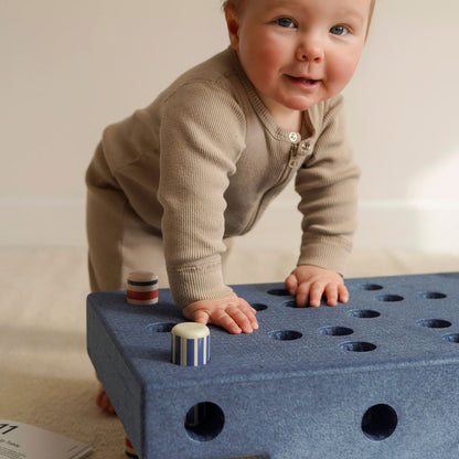 Peuter kruipend op MODU Baby Activity Set in diepe blauw, speelgoed met gaten en houten poppetjes zichtbaar