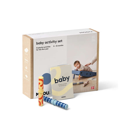 MODU Baby Activity Set verpakking met twee speeltjes ernaast, op houten ondergrond met baby die speelt