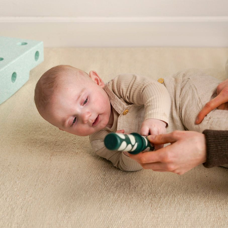 MODU Baby Activity Set in Ocean Mint en Forest Green: newborn speelt met groene gestreepte sok terwijl volwassene ondersteunt
