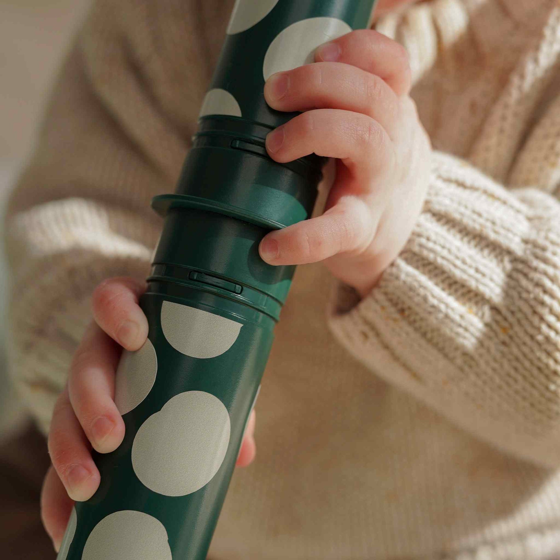 MODU Baby Activity Set Forest Green met witte stippen, vastgehouden door baby's handjes in crème gebreide kleding