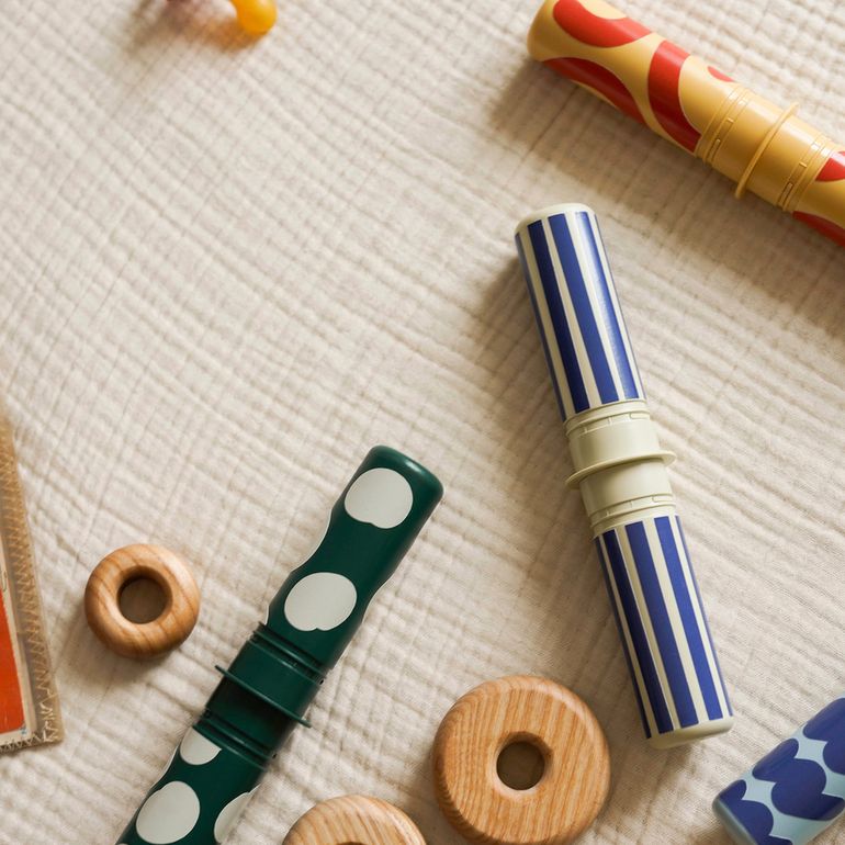 MODU Baby Activity Set speelgoed flat lay met houten ringen, gekleurde rammelaars en gestreepte buizen op neutraal textiel